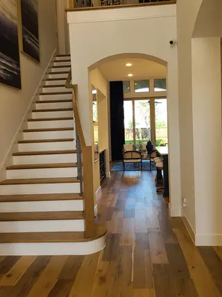 Model Home A welcoming hallway with elegant wood flooring, a stylish staircase, and ample natural light pouring through large windows.