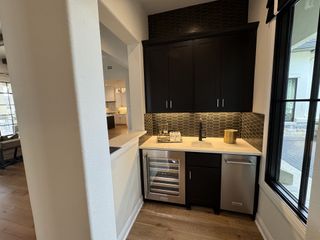 A chic wet bar featuring sleek black cabinets, a wine cooler, and modern hexagonal backsplash tiles.