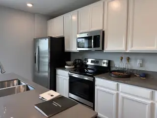 A modern kitchen with sleek stainless appliances, white cabinetry, and a quartz countertop.