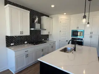 A modern kitchen with white cabinets, black herringbone backsplash, marble island, and pendant lighting.