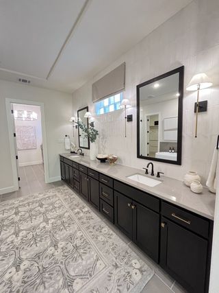 A sleek bathroom featuring a long vanity with dual sinks, elegant mirrors, and a patterned rug for a touch of luxury.