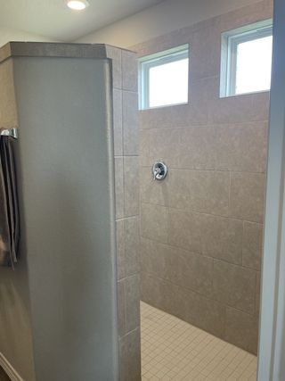 Model Home A spacious walk-in shower with floor-to-ceiling tile and natural light from high windows.