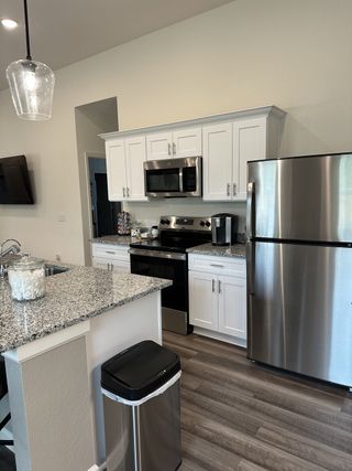 Model Home A modern kitchen with white cabinets, stainless steel appliances, gray granite countertops, and sleek lighting fixtures.
