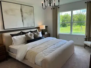 A serene bedroom with a plush bed, abstract art, and large window overlooking lush greenery. Modern lighting and neutral tones.