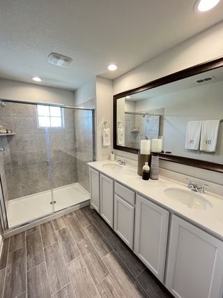Model Home A modern bathroom with a sleek double vanity, spacious glass shower, and stylish wood-look flooring.
