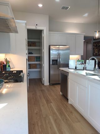 A modern kitchen with sleek stainless appliances, white cabinetry, open shelving, and wood flooring.
