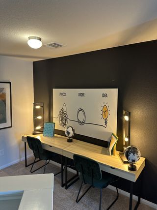 A modern workspace with a black accent wall, dual desk, globe decor, and stylish lighting.