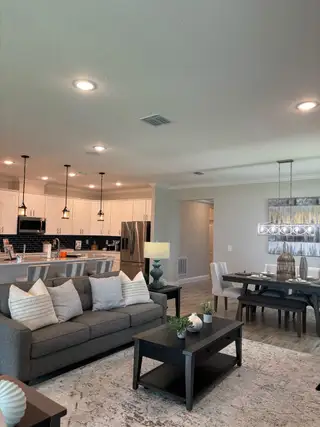 An inviting open-concept living space with a cozy gray sofa, sleek kitchen island, and chic dining area with elegant lighting.