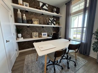 Model Home A modern office with a sleek desk, decorative shelving, wood accents, and abundant natural light.