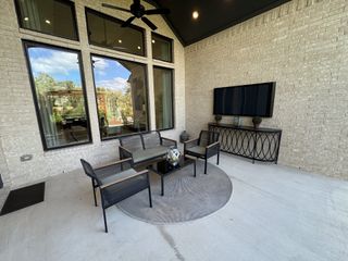 Model Home A cozy outdoor patio with sleek black furniture, large windows, and a TV mounted on a brick wall.