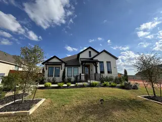 Street view Exterior – A charming modern farmhouse-style home with elegant landscaping in Crosswinds by Perry Homes (Kyle, TX).