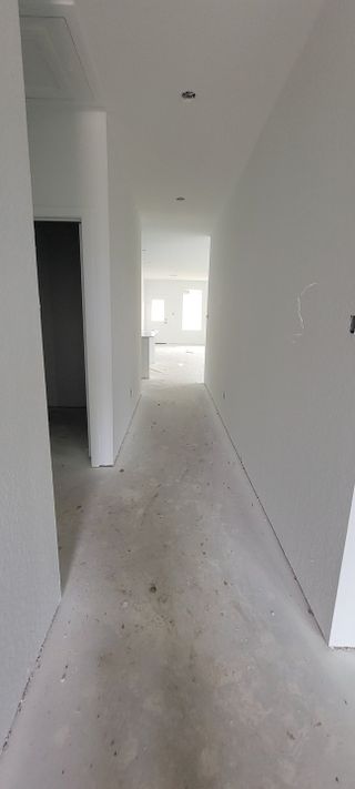 A long hallway in an under-construction home, leading to a bright open space at the far end.