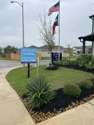Street view Lush landscaping greets visitors at Hacienda by Century Communities in San Antonio, TX, showcasing prideful flora and signage.