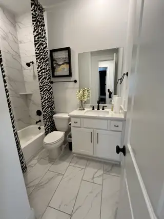A chic bathroom with marble-patterned tiles, sleek black fixtures, and a playful zebra shower curtain for a stylish touch.