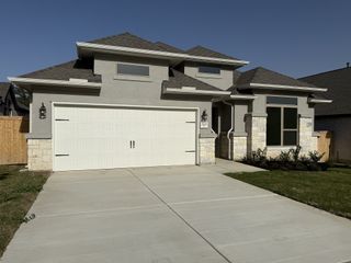 A modern gray home with white stone accents and manicured lawn in Ladera by Coventry Homes (San Antonio, TX).