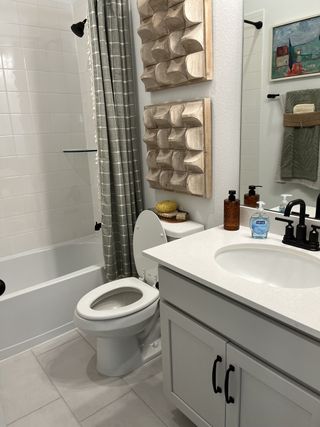 A modern bathroom with white cabinetry, a sleek countertop, geometric wall decor, and a tiled shower area.