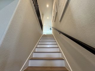 Street view A sleek staircase with wooden treads, smooth walls, and modern railing leads to an airy upper floor with ceiling fan.