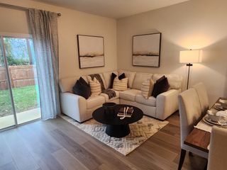 A cozy living room with a beige sectional, modern art, and warm lighting, adjacent to a dining area and patio view.