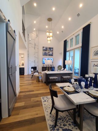 Model Home A spacious living area with high ceilings, chic lighting, and elegant dining set on hardwood floors.