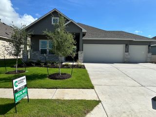 Street view A charming gray home with a neat lawn and three-car garage in Carillon by Chesmar Homes (Manor, TX).