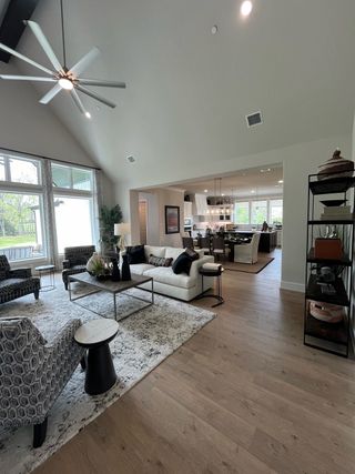 A spacious living area with modern furnishings, high ceilings, large windows, and an open layout leading to a chic kitchen.