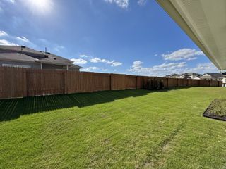 A spacious backyard with lush green grass and a wooden fence in Crosswinds by Milestone Community Builders (Kyle, TX).
