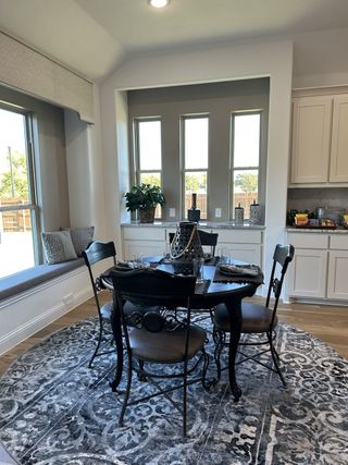 A cozy dining nook featuring a round table, elegant chairs, and large windows, with a stylish gray-patterned rug.