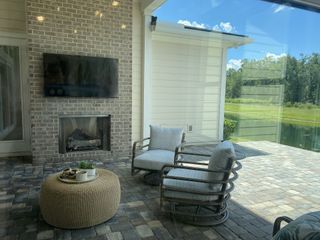 A cozy patio with a brick fireplace, mounted TV, and comfy seating overlooking a tranquil pond.