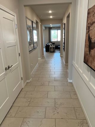 A bright hallway with tiled flooring, neutral walls, and elegant artwork, leading to a cozy living area filled with natural light.