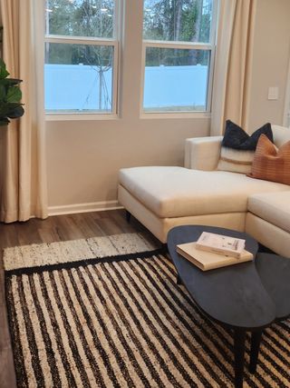 A cozy living space with a sectional sofa, striped rug, and chic coffee table under large windows.