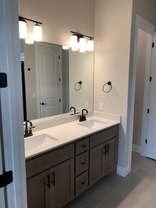 Contemporary bathroom with dual sinks, sleek black fixtures, wood cabinetry, and elegant lighting over a large mirror.