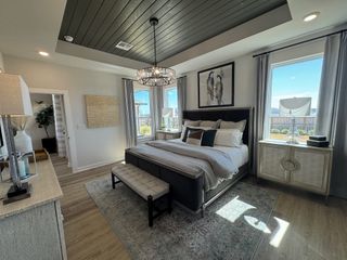 A sophisticated bedroom with elegant bedding, a stylish chandelier, and large windows letting in natural light.