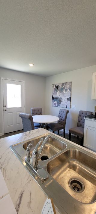 Model Home A modern dining nook with gray chairs, a round white table, and abstract wall art, adjacent to a sleek dual kitchen sink.