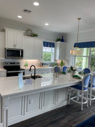 A modern kitchen with white cabinetry, large island, stainless steel appliances, and elegant blue accents.