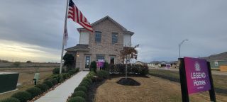 Charming brick home with a neat lawn and flag display in Blue Ridge Ranch by Legend Homes (San Antonio, TX).
