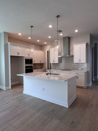 Sleek kitchen with white cabinets, elegant island, stainless steel appliances, and modern lighting on wood floors.