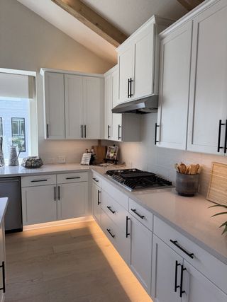 A modern kitchen featuring sleek white cabinetry, a gas cooktop, and ambient lighting with elegant wood beam accents.