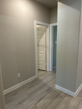 A modern hallway featuring sleek wood-look tile flooring and crisp light gray walls.