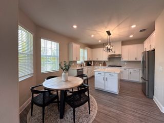 A modern kitchen with white cabinetry, a round dining table, sleek pendant lighting, and light wood floors.