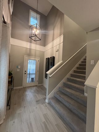A spacious entryway featuring a chic pendant light, tile flooring, and carpeted stairs.