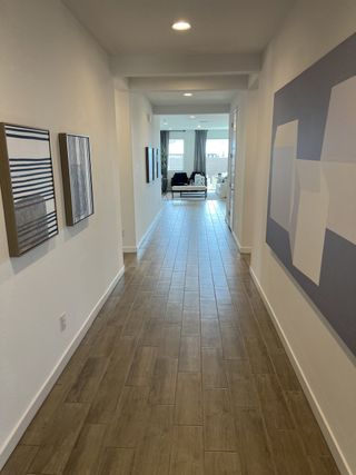 A bright hallway with wood tile flooring, modern art pieces, and a glimpse of a stylish living room at the end.