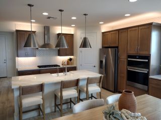 A modern kitchen featuring wood cabinets, a sleek island, stainless steel appliances, and elegant pendant lighting.