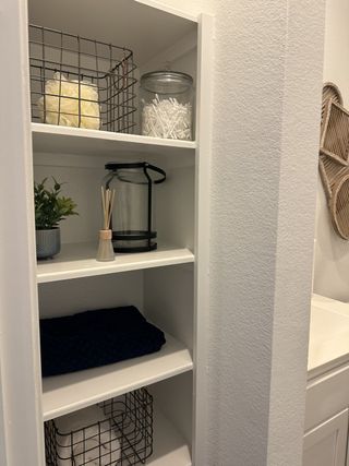 Organized bathroom shelving with neatly arranged baskets, glass jars, a plant, and a folded towel for a tidy aesthetic.