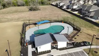 A modern community pool with shade structures in EastVillage - Classic Collection by KB Home (Manor, TX).