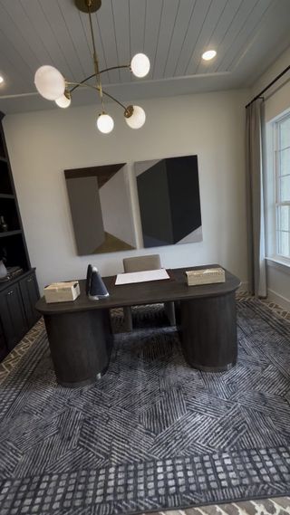 A contemporary home office featuring abstract art, a sleek desk, ambient lighting, and a patterned rug.