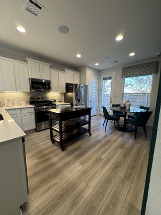 Model Home A modern kitchen with sleek white cabinets, stainless steel appliances, wood flooring, and an inviting dining area.