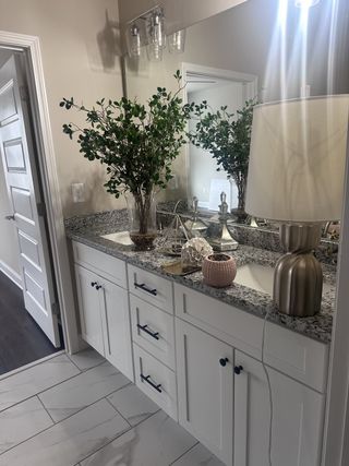 Model Home A chic bathroom with a granite countertop, white cabinetry, and elegant decor accents.