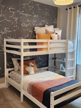 A cozy children's room with a white bunk bed, constellation-themed wall, and plush toys.