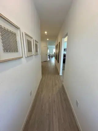 Model Home A bright hallway with wood flooring and framed art leads to a cozy living area, creating a welcoming atmosphere.