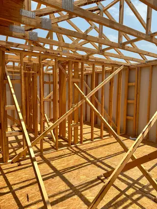 A home under construction showcasing wooden framing and trusses, highlighting early building stages and architectural progress.